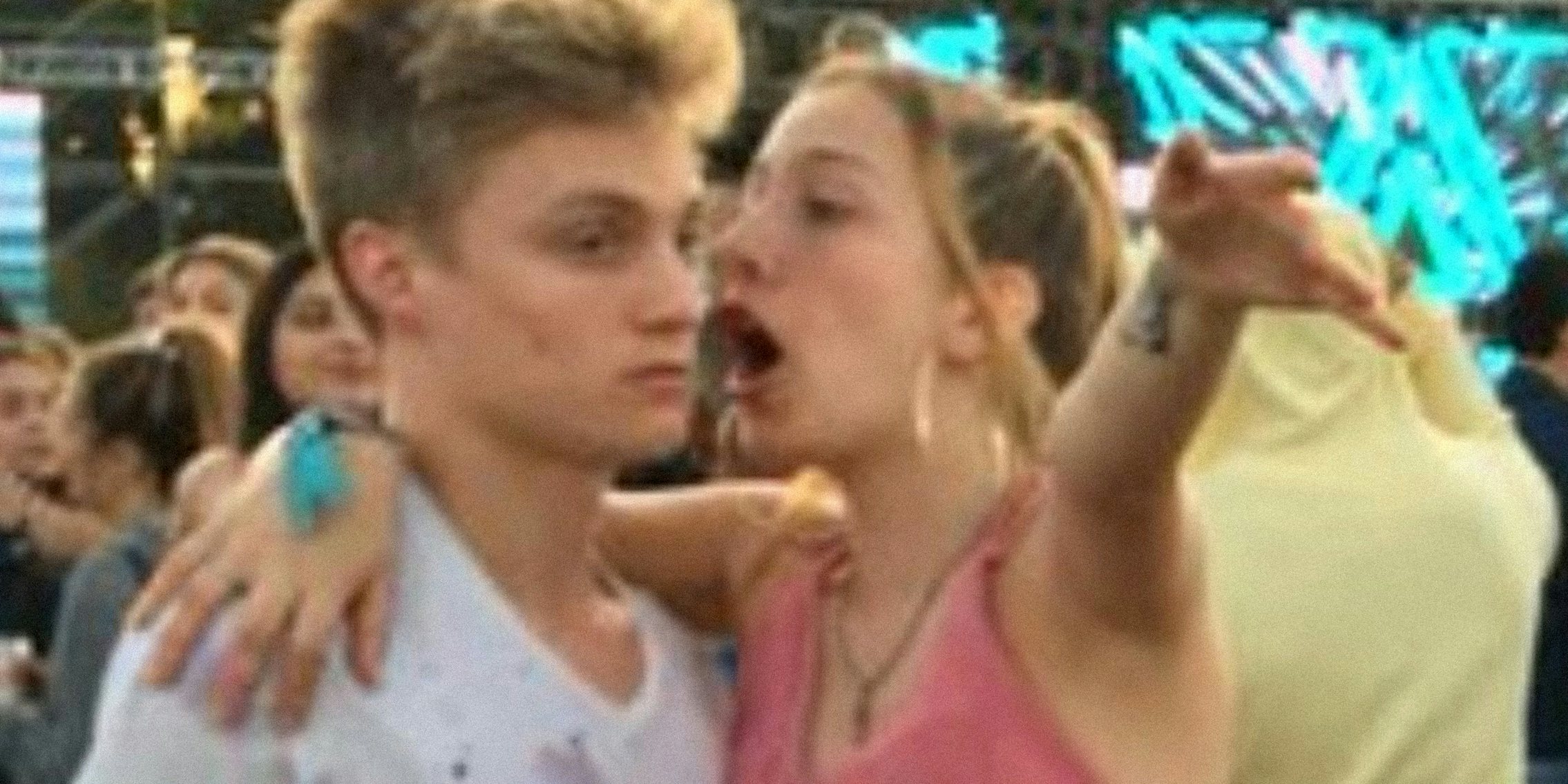 young woman with arm around a young man, speaking to him in a crowd