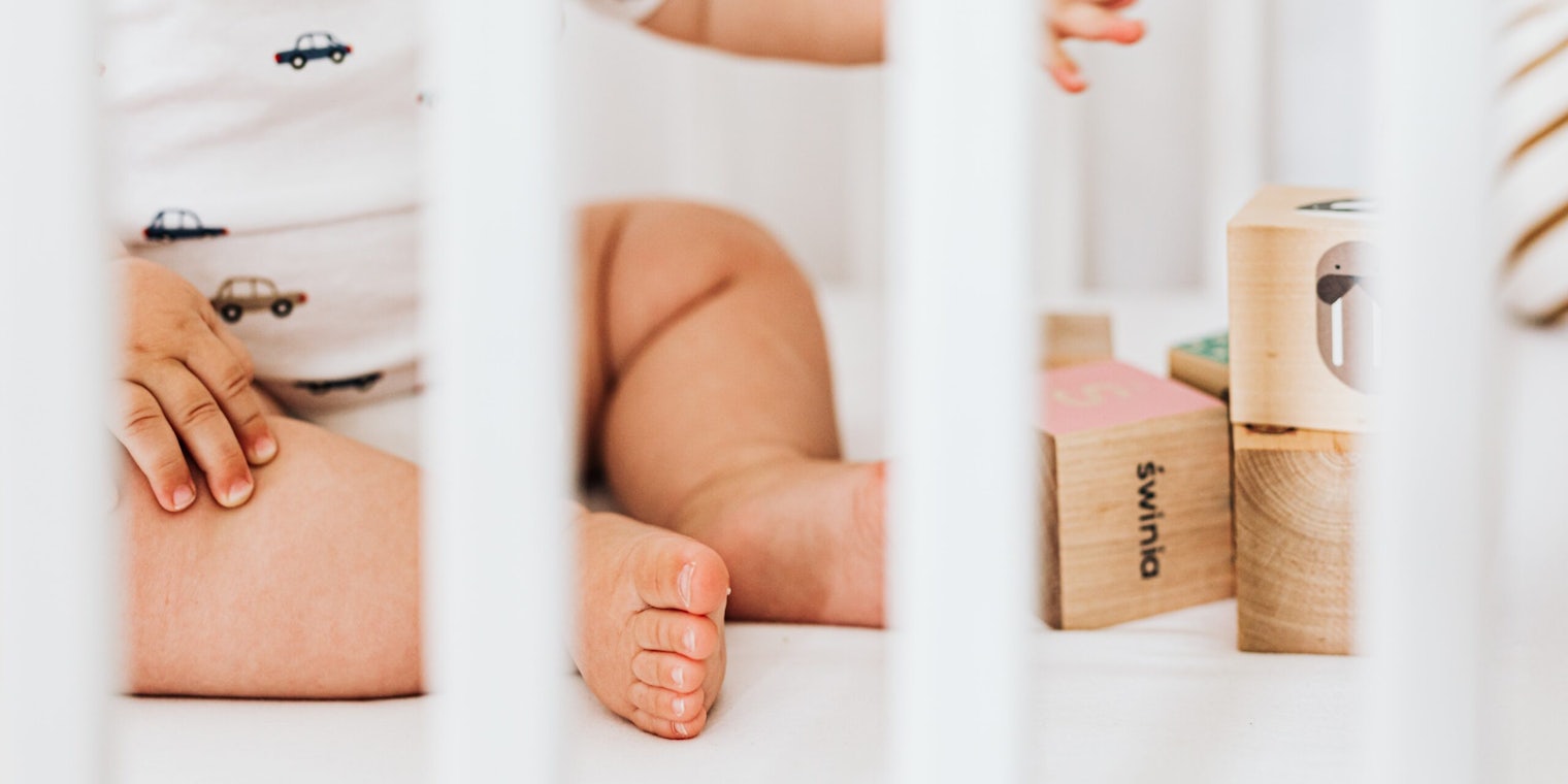 Baby in crib playing with wooden blocks.
