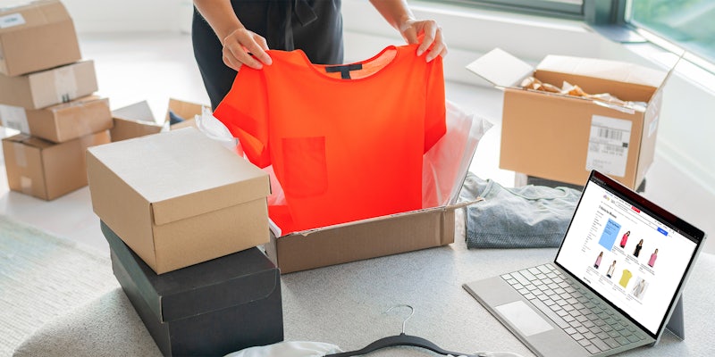 woman packing shirt into box with eBay listing on laptop