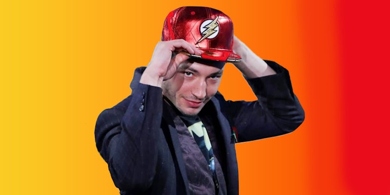 Ezra Miller posing with Flash logo hat on yellow to red gradient background