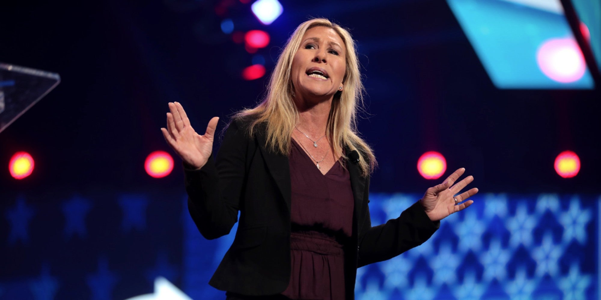A blonde haired woman on a stage giving a speech