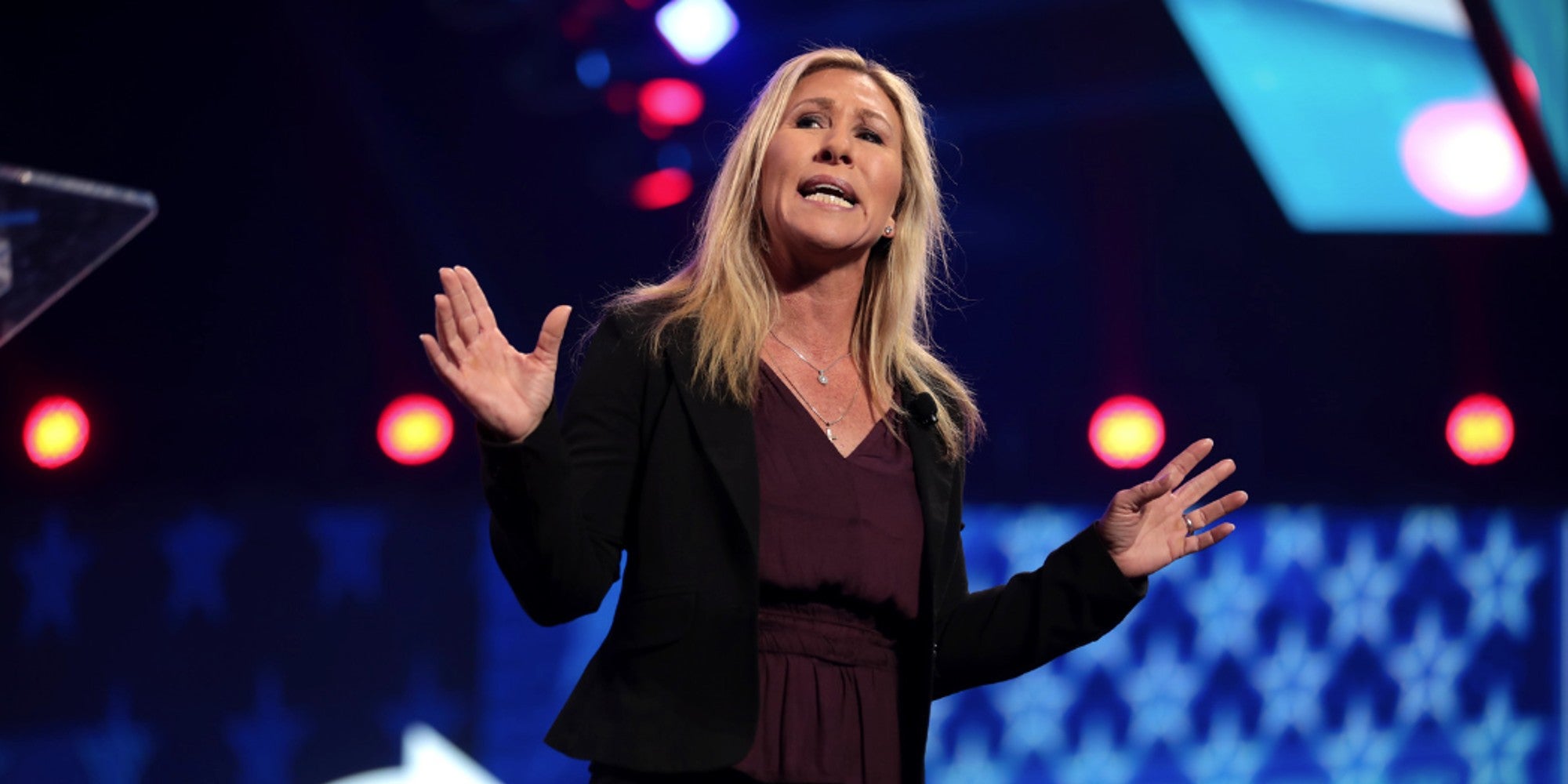 A blonde haired woman on a stage giving a speech