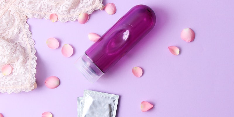 lubricant bottle and a condom on a pink background with the corner of a bra peaking out