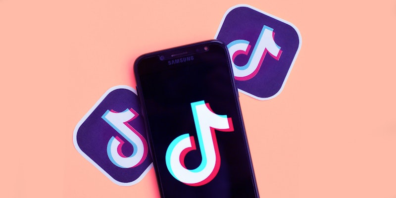 TikTok logo on black phone with TikTok logo stickers on light pink background