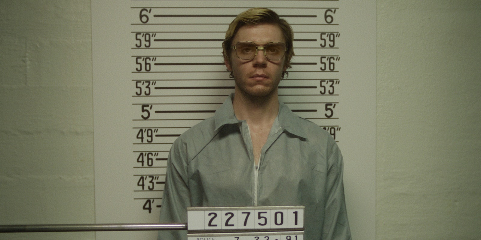 Evan Peters standing against a wall posing for his mug shot in the Dahmer series