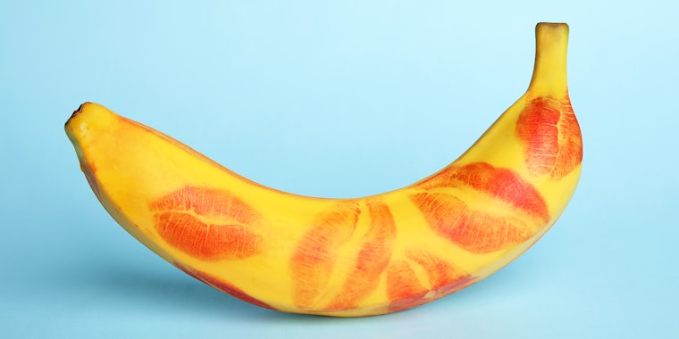 Fresh banana with red lipstick marks on blue background
