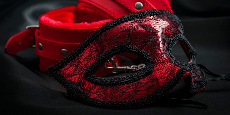 close up on erotic mask and red handcuffs isolated on black silk background