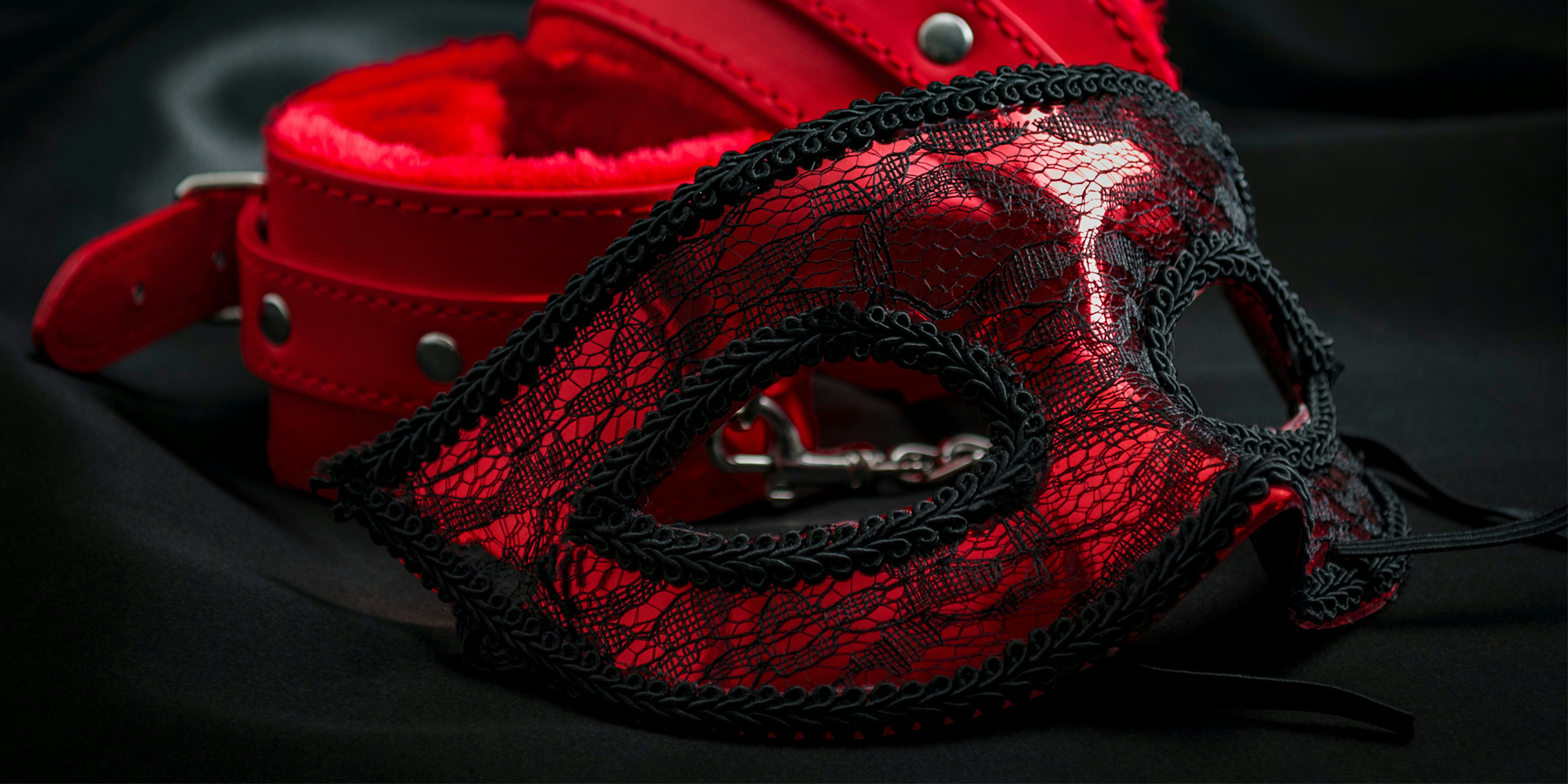 close up on erotic mask and red handcuffs isolated on black silk background