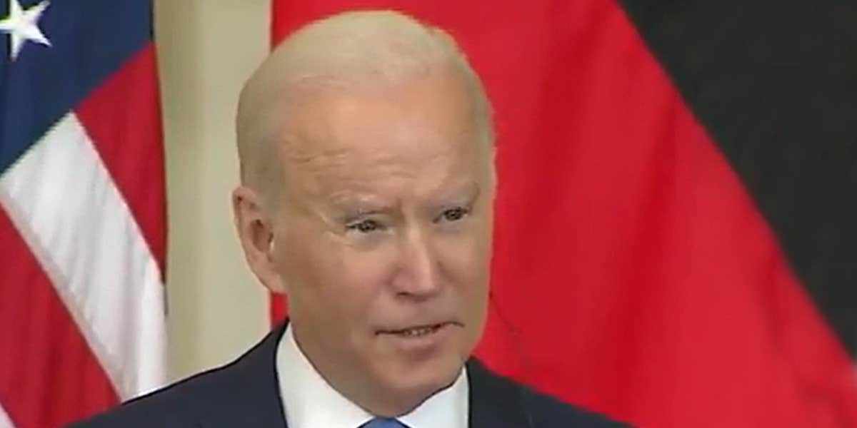 Joe Biden speaking in front of red tan and black background with American flag