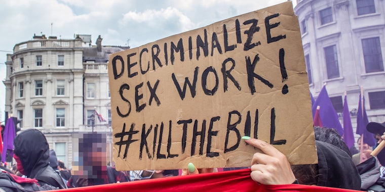 protesters outside woman holding sign 'DECRIMINALIZE SEX WORK! #KILLTHEBILL'