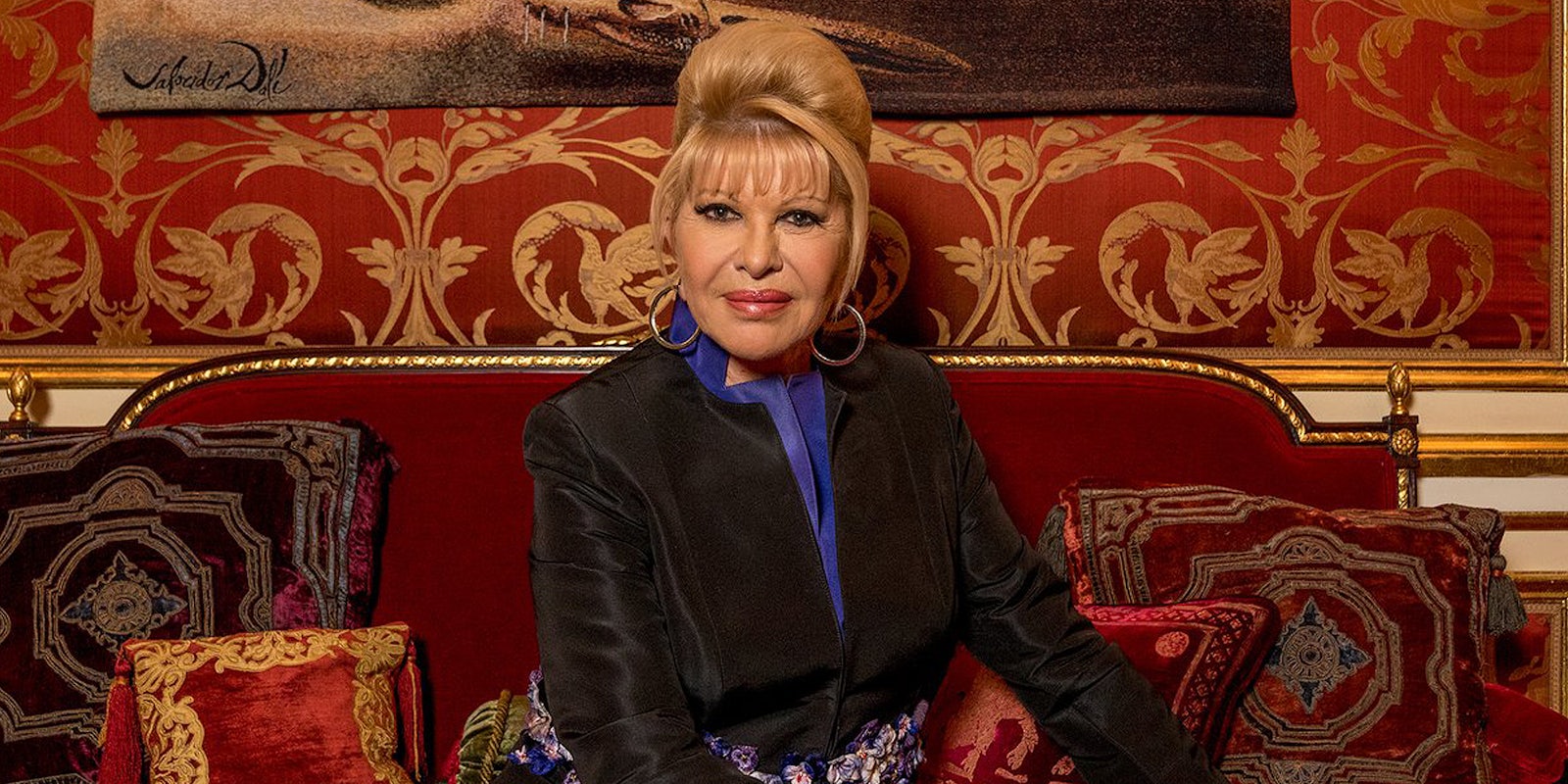 Ivana Trump sitting on red couch with red wall and painting behind her