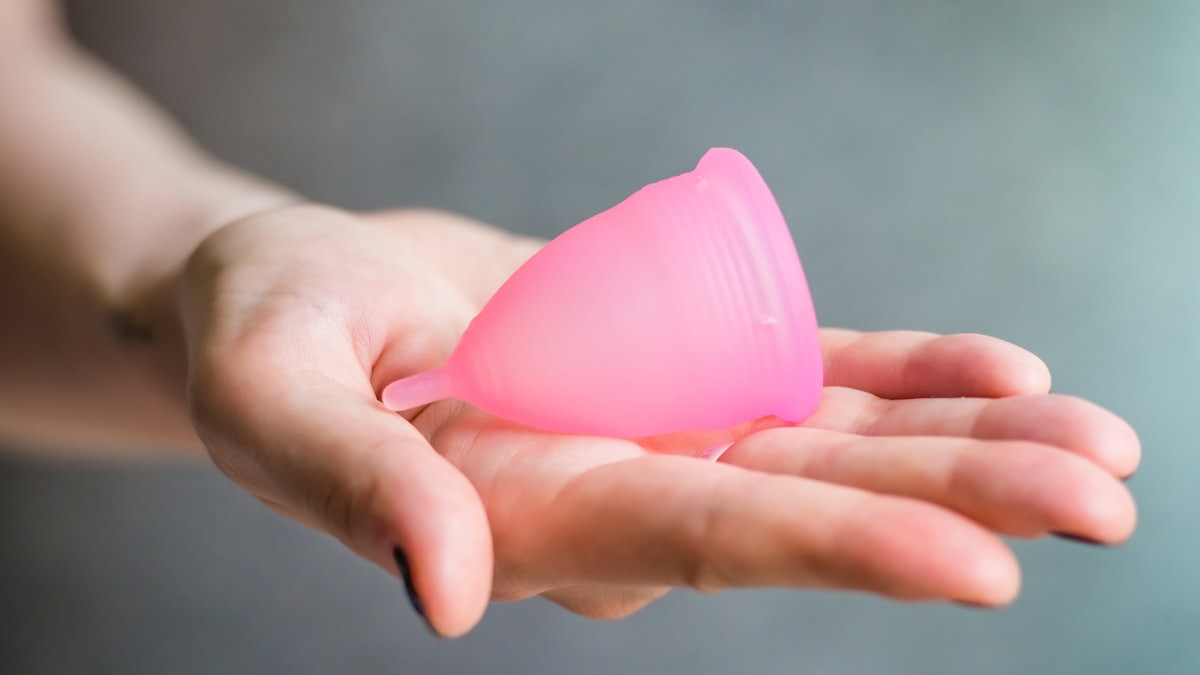 pink menstrual cup in hand in front of gray background