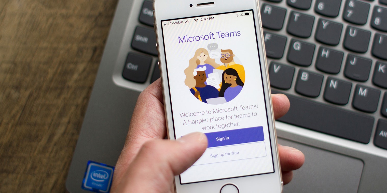 A user opens the Microsoft Teams mobile app with laptop in the background