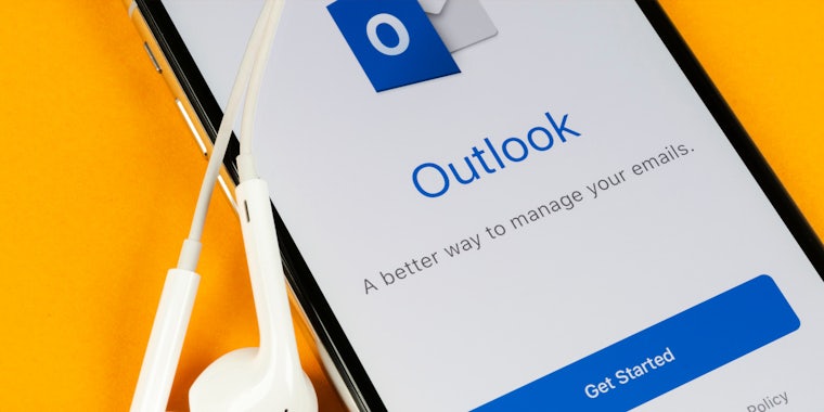 Outlook app open on cell phone with earbuds on yellow background