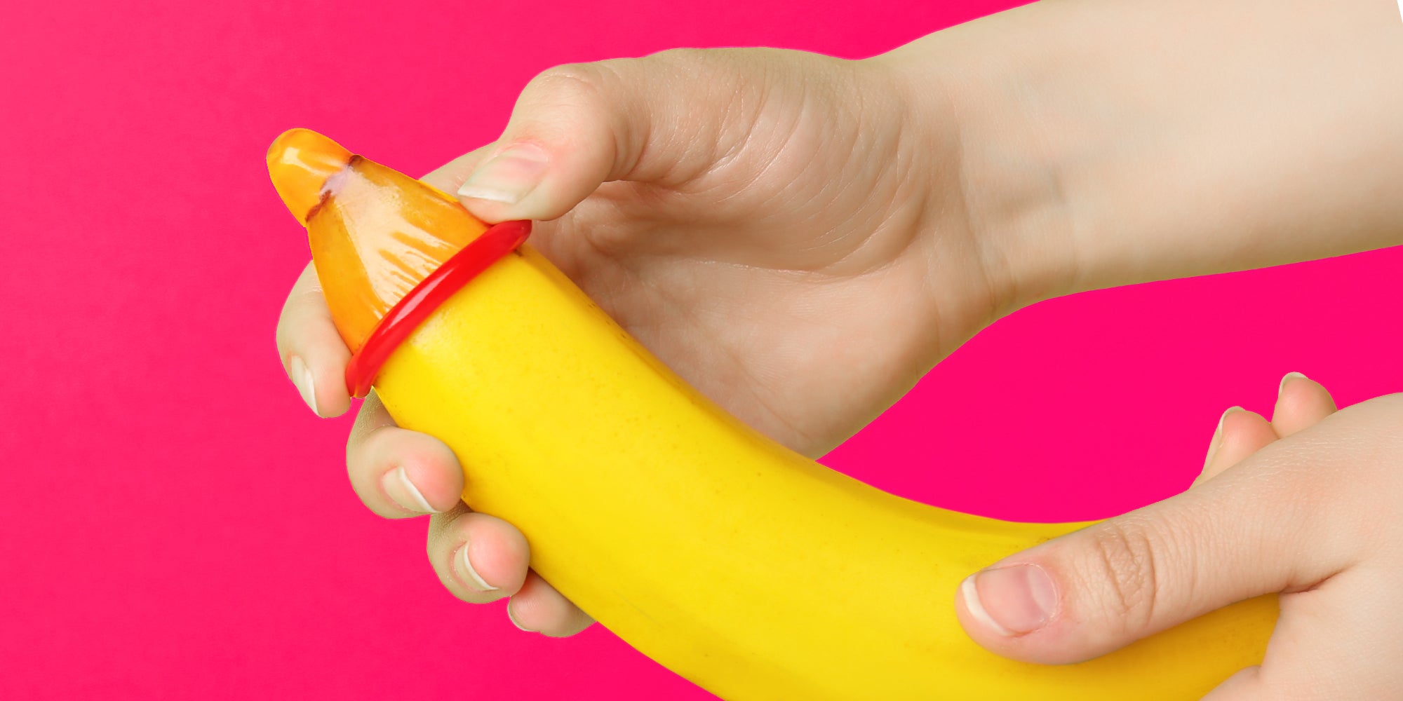 Woman putting condom on banana against color background