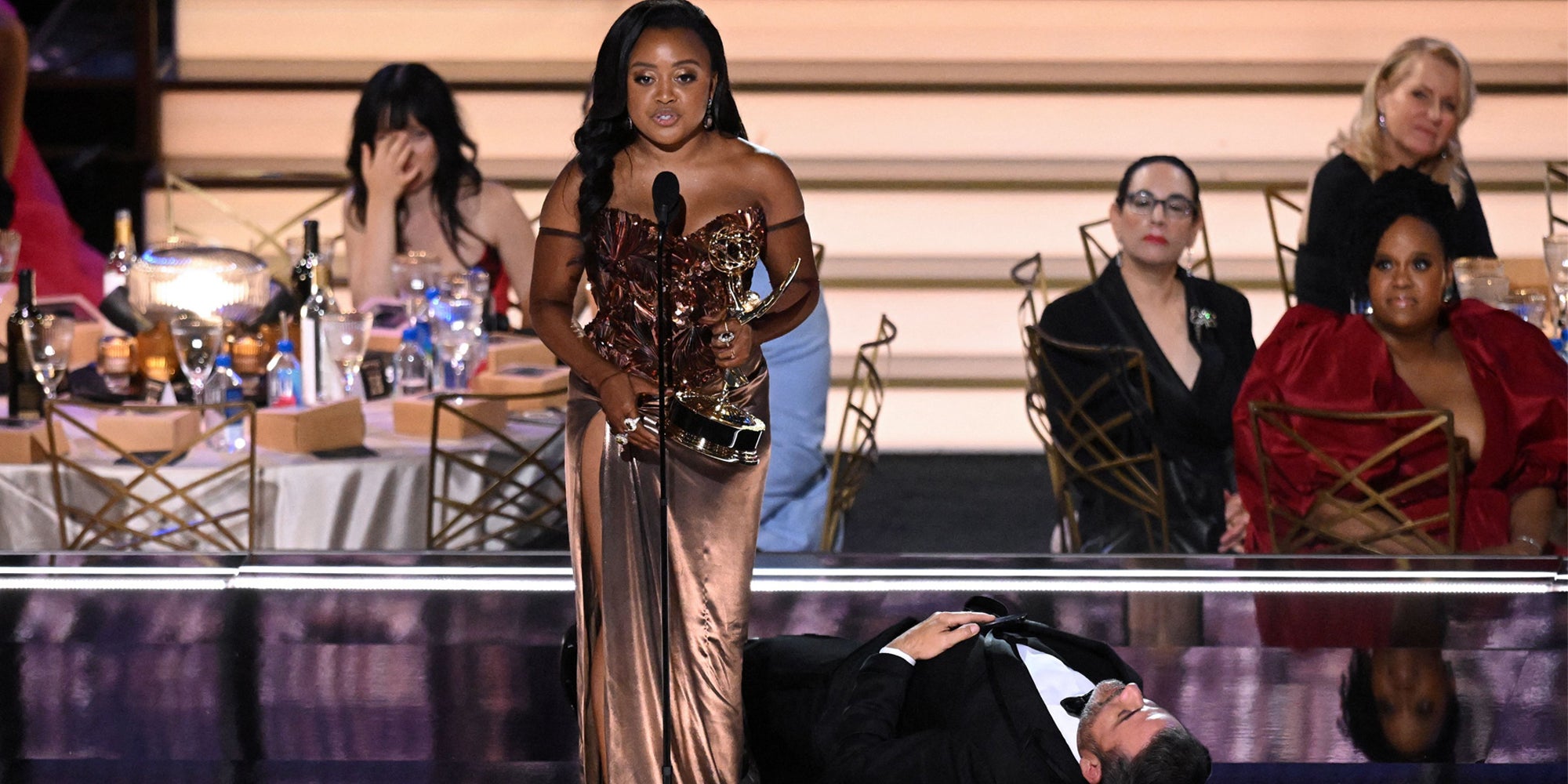 Jimmy Kimmel laying on stage next to Quinta Brunson during her Emmy's speech while others are behind