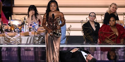 Jimmy Kimmel laying on stage next to Quinta Brunson during her Emmy's speech while others are behind
