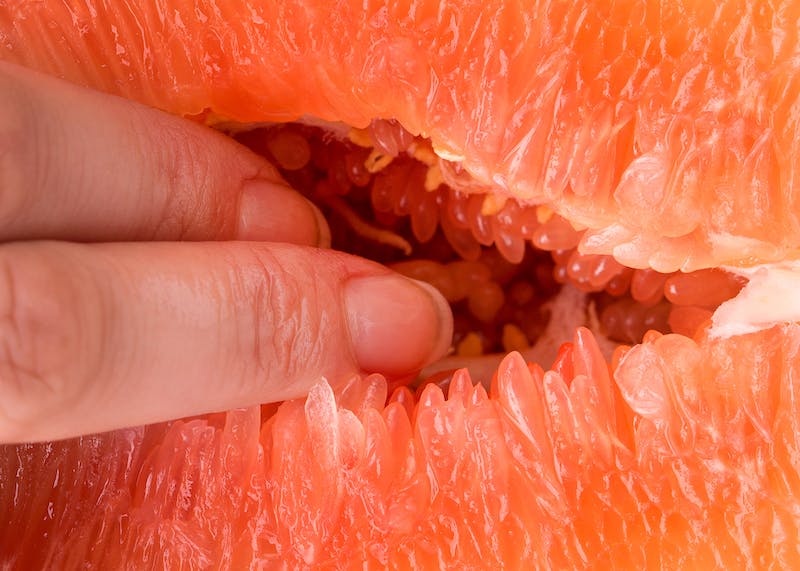 Fingers inserting themselves into a grapefruit