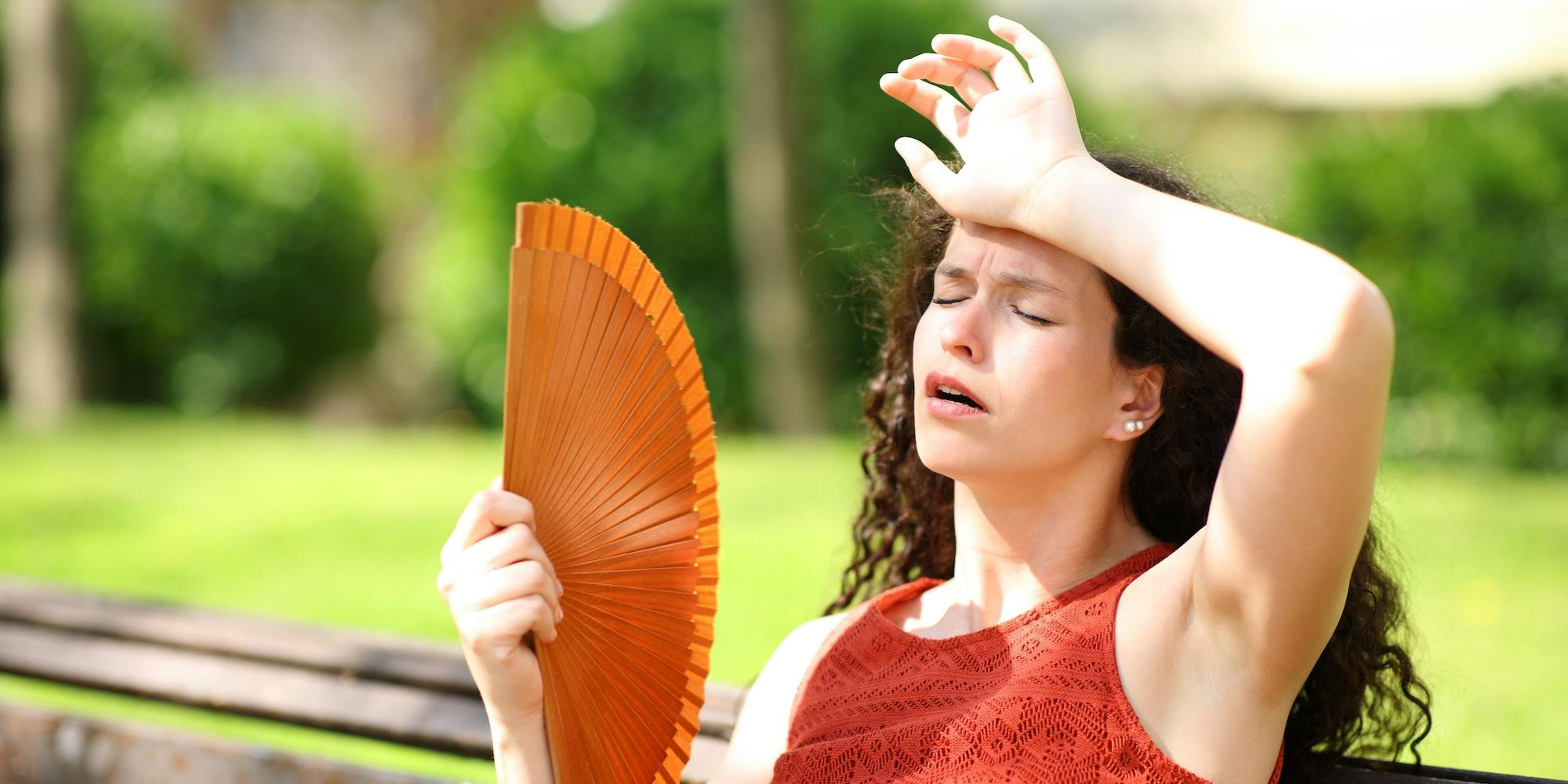 Woman in a park suffering heat stroke fanning herself with a red fan.