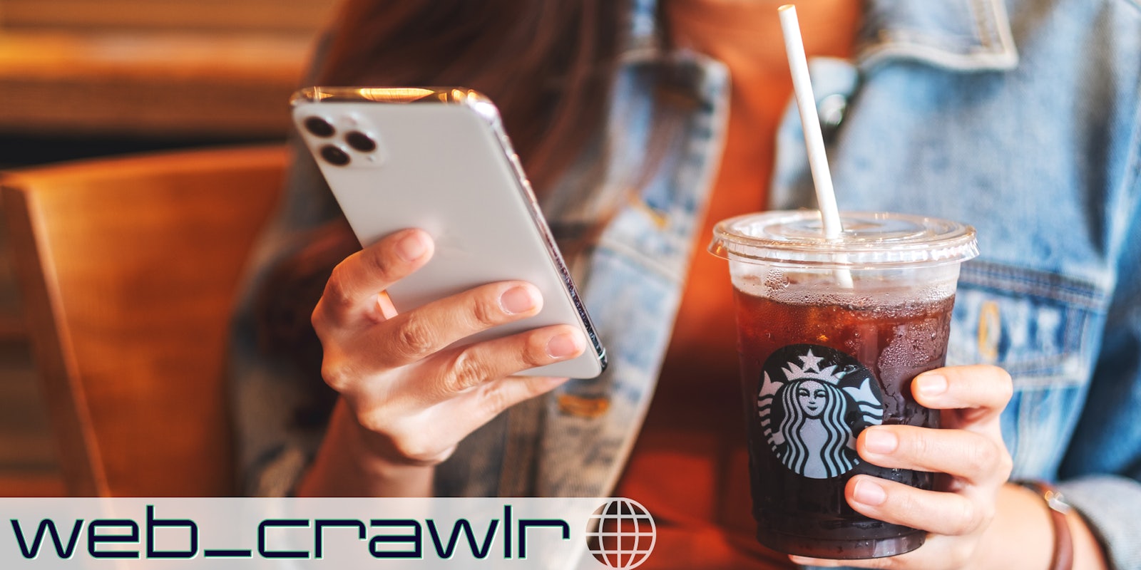 A person holding a smartphone and Starbucks coffee. The Daily Dot newsletter web_crawlr logo is in the bottom left corner.