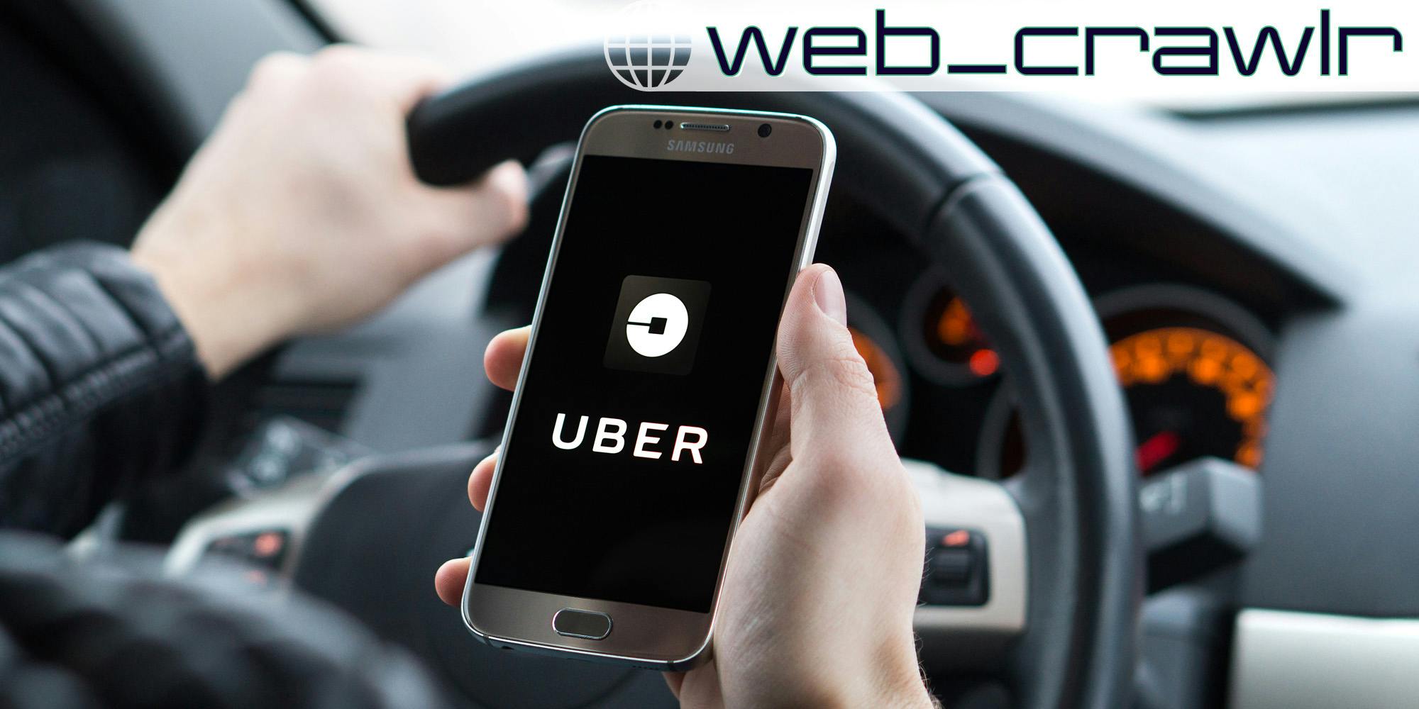A person driving a car and holding a smartphone with the Uber logo on it. The Daily Dot newsletter web_crawlr logo is in the top right corner.