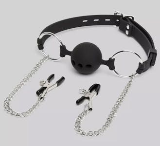 Dominix deluxe ball gag with attached nipple clamps against a grey background.