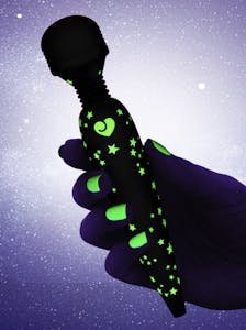 A hand with glow-in-the-dark nail polish holding the Lovehoney Glow in the Dark Deluxe Mini showing off its glowing decals against a starry background.