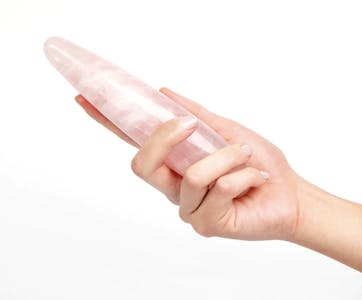 A hand holding the Chakrubs rose quartz wand against a white background.