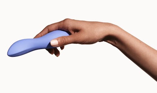 A hand holding a periwinkle Dame dip vibrator against a beige background.