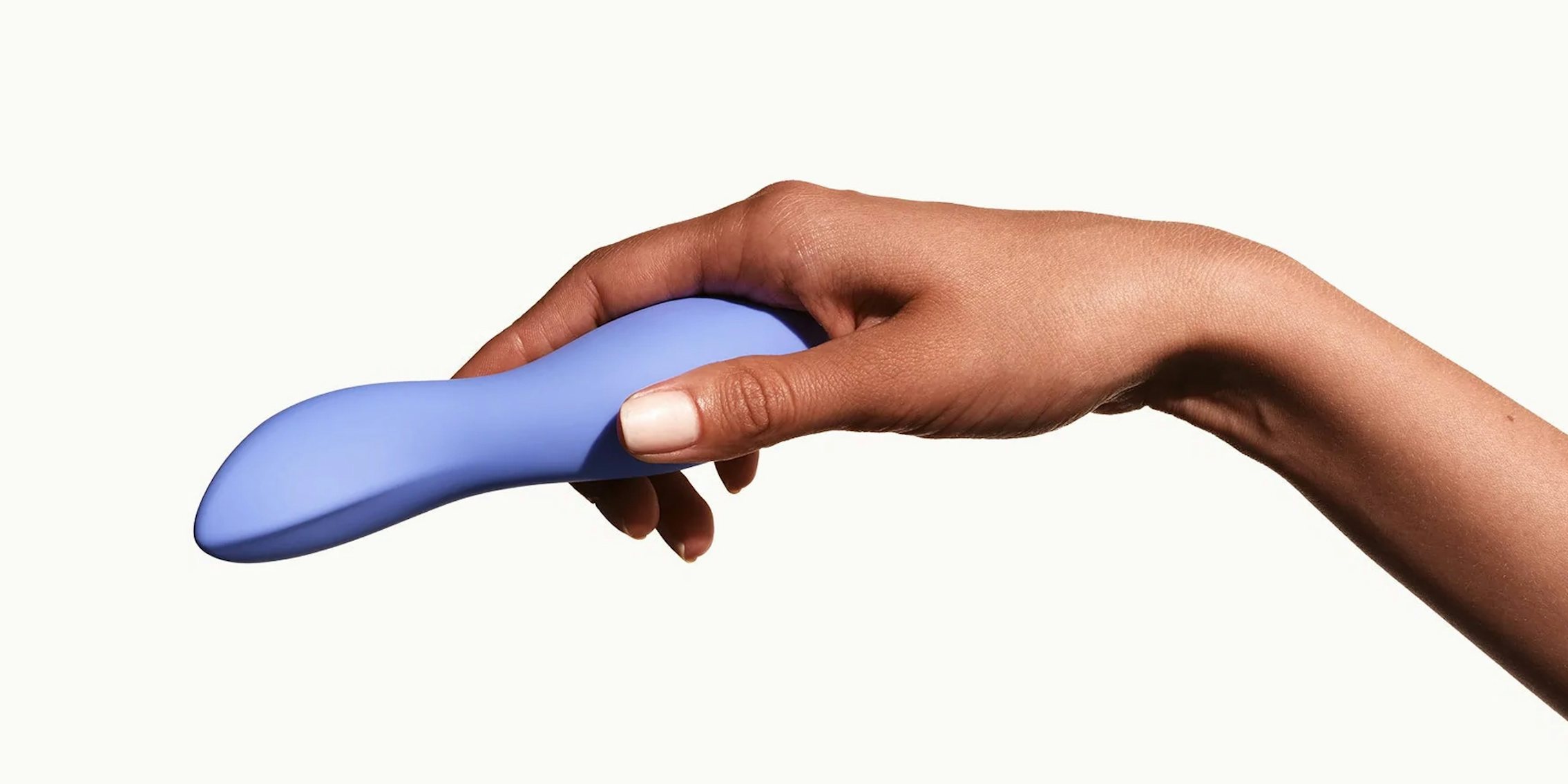 A hand holding a periwinkle Dame Dip vibrator against a beige background.