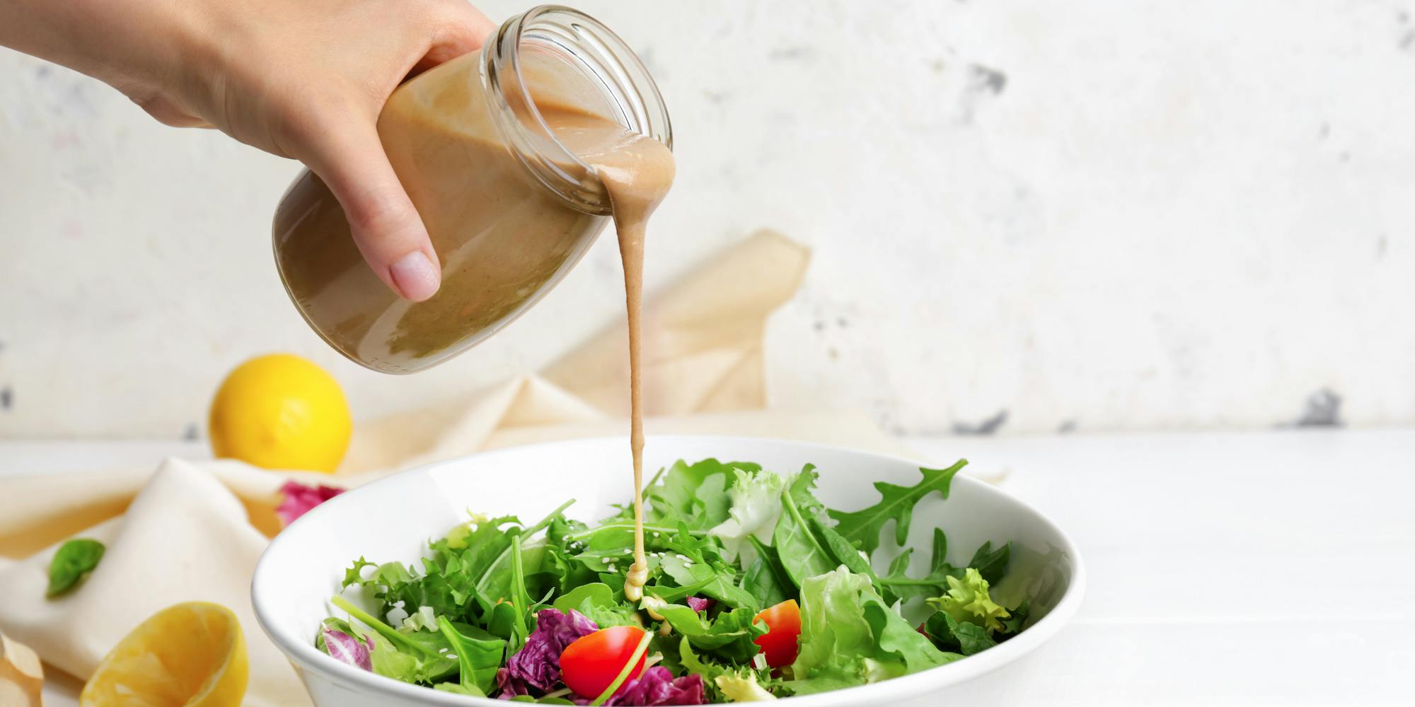 woman pouring salad dressing on a salad