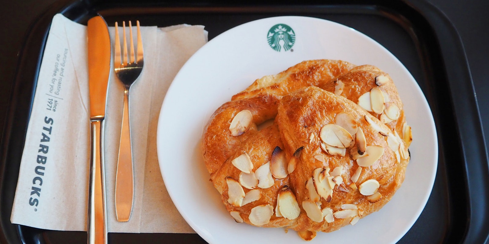 Starbucks Almond Croissant on Starbucks plate on black food tray
