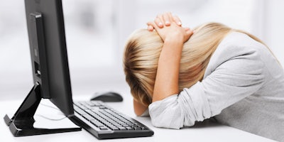 A woman leaning on her desk with her hands over her head in front of a computer.