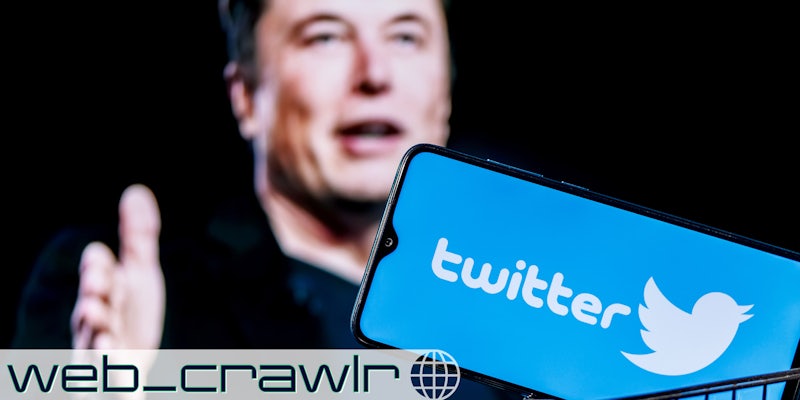Elon Musk in front of a smartphone with the Twitter logo on it. The Daily Dot newsletter web_crawlr logo is in the bottom left corner.