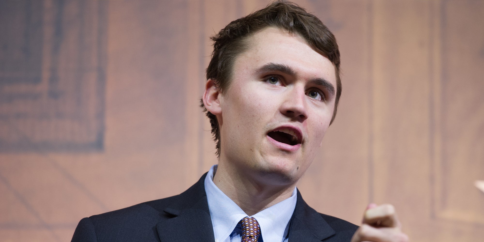 Charlie Kirk speaking in front of tan background