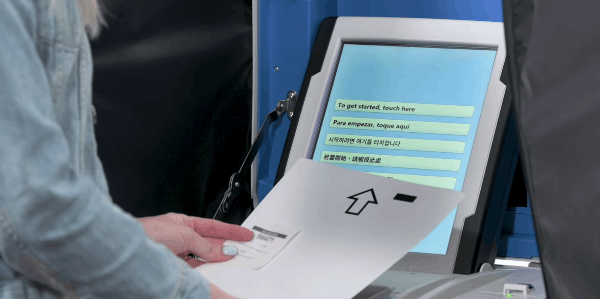 A woman inserting a piece of paper into a voting machine