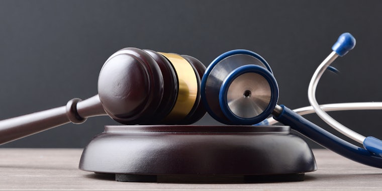 wooden gavel with stethoscope in front of gray background