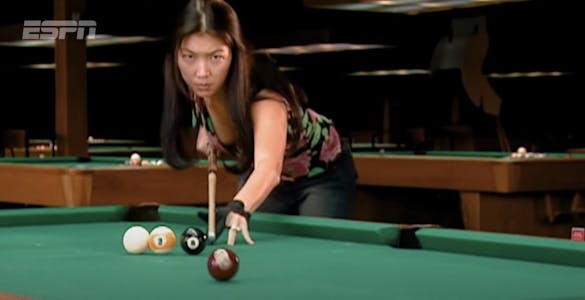 A focused Jeanette Lee leaning over a pool table shoots the seven ball with her cue from a line of other pool balls.