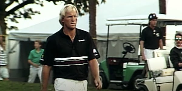 A screenshot from the 2022 ESPN documentary "Shark" showing golfer Greg Norman walking on a golf course with people and golf carts in the background.