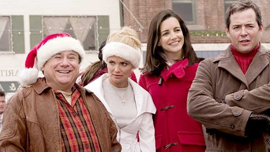 Danny DeVito smiling in a Santa hat and Matthew Broderick crossing his arms with two women between them.