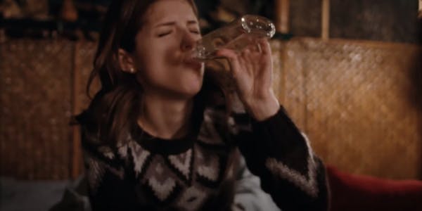Anna Kendrick in a sweater drinking from an empty bottle of liquor.
