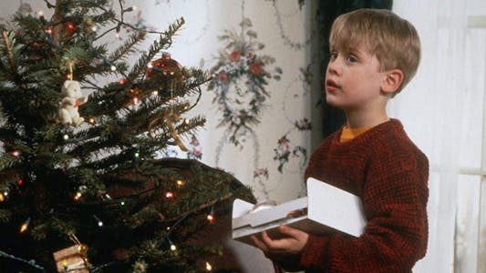 best Christmas movies streaming - Macaulay Culkin standing by a Christmas tree and holding a box.