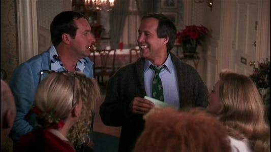 best christmas movies streaming - Chevy Chase smiling at Randy Quaid while holding an envelope as the rest of the Griswold family looks on.