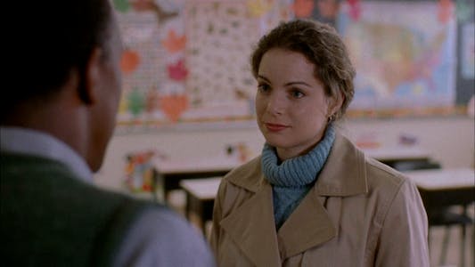 A woman wearing a winter coat in a classroom looking at a man.