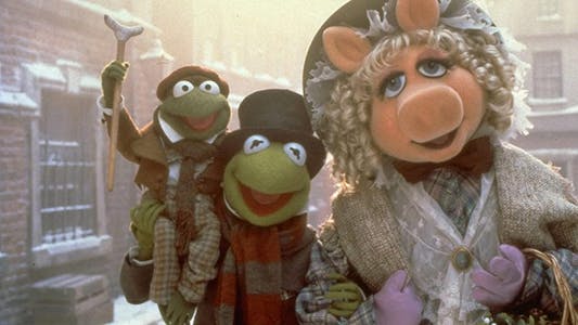 best Christmas movies streaming - Kermit the Frog and Miss Piggy dressed in Victorian clothing while Kermit holds a smaller frog carrying a crutch like Tiny Tim.