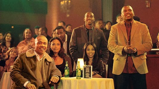 best Christmas movies streaming - Two men standing and a man sitting at a table with two women while watching some kind of performance out of frame.