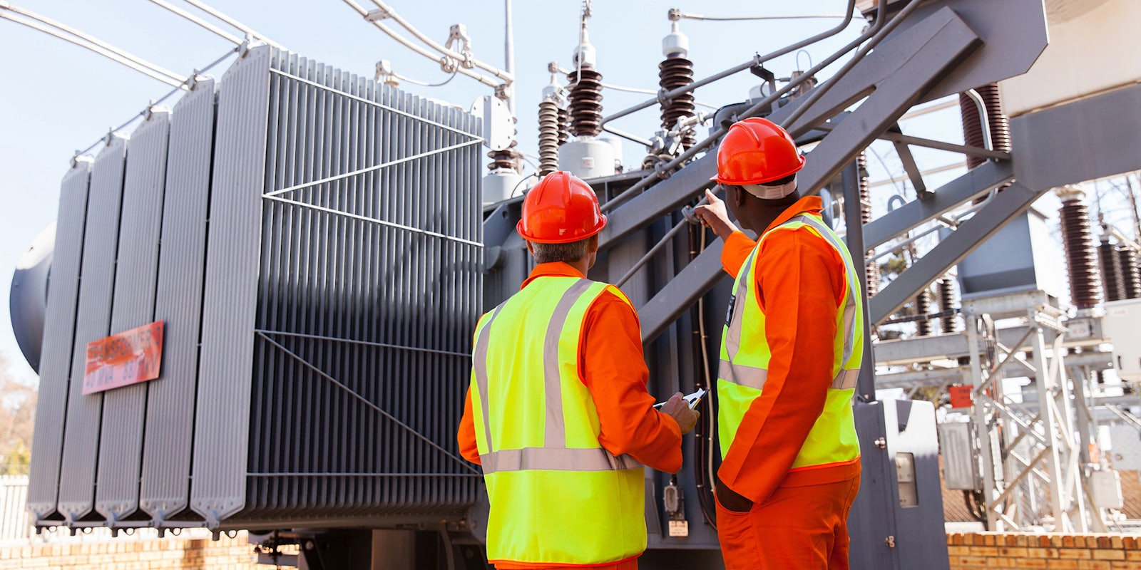 back view of electricians standing next to a transformer in electrical power plant
