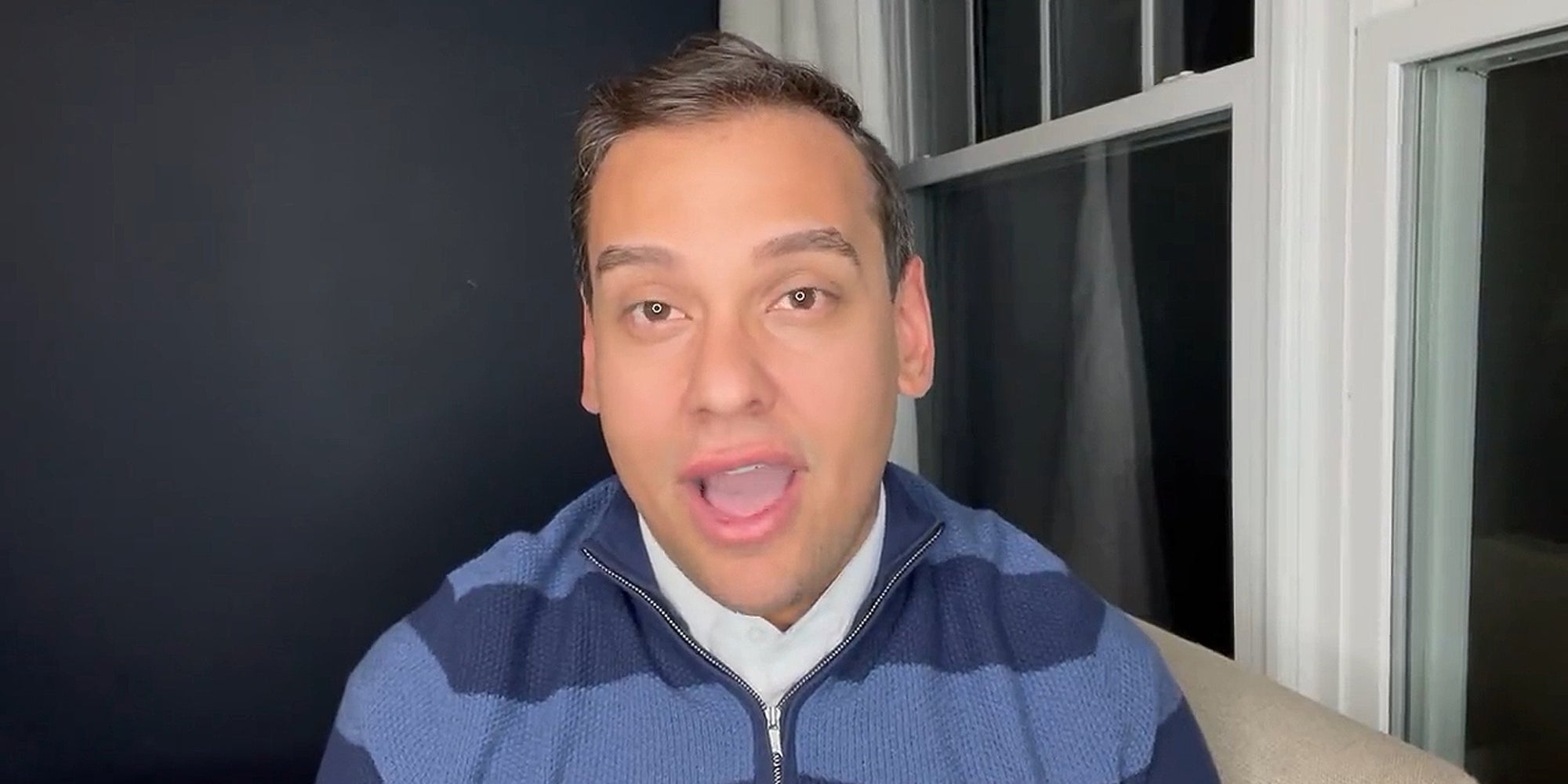 George Santos speaking in chair in front of gray wall and windows