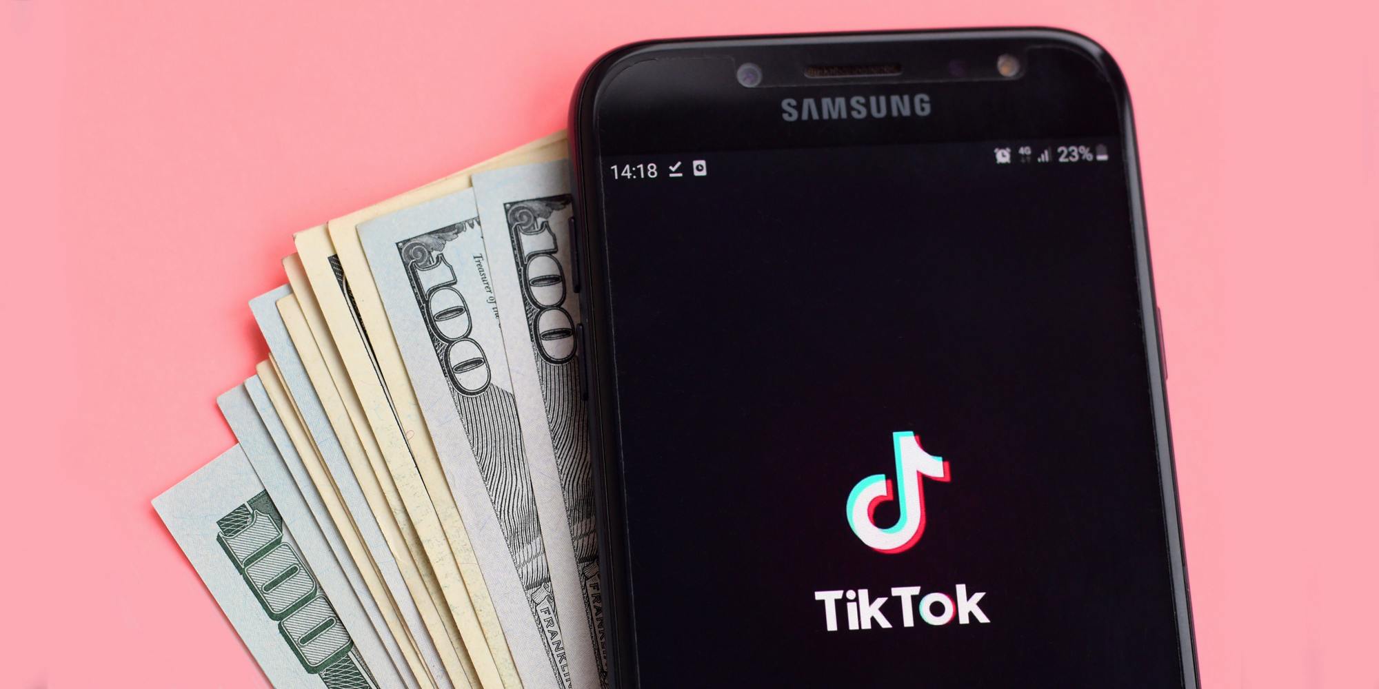 TikTok on phone with money in front of pink background