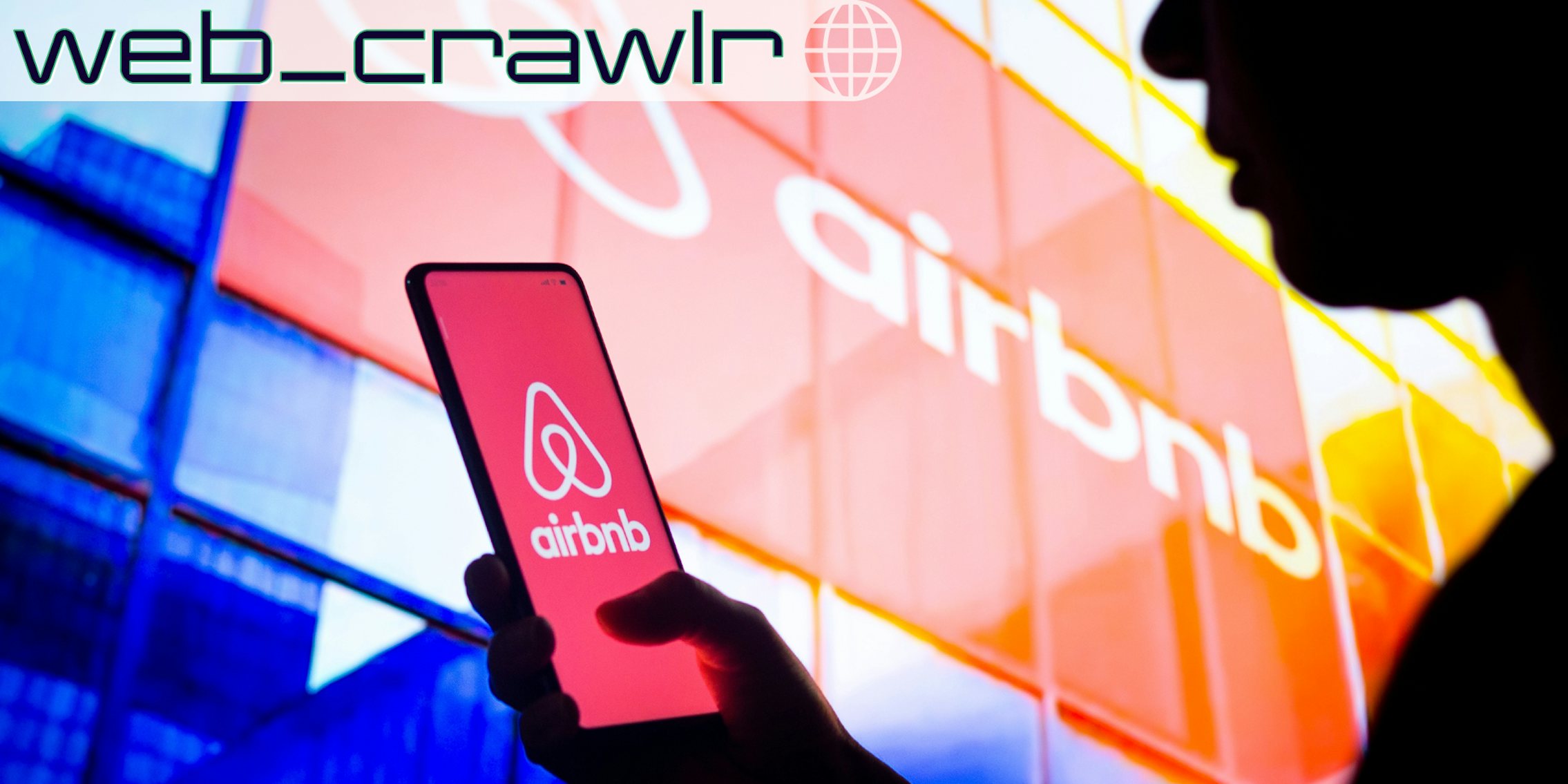 A person holding a phone with the Airbnb logo on it. The Daily Dot newsletter web_crawlr logo is in the top left corner.